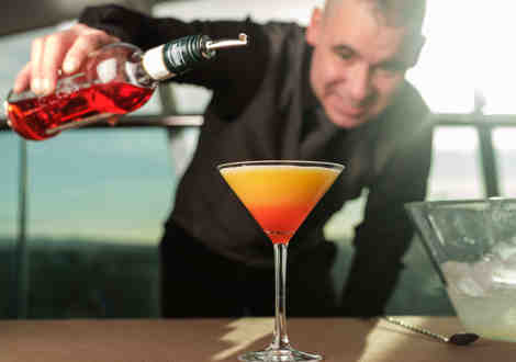 A waiter pouring a bottle to create an orange cocktail.